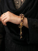 Close-up of a hand wearing a gold bracelet with dark beads against a black garment.